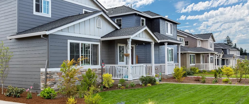 A charming two-story house with a white front porch, blue-gray siding, and a lush green yard.