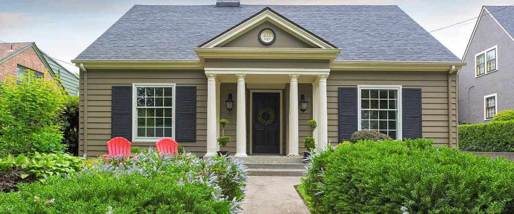 A traditional-style home with yellow siding, black shutters, white columns, and a landscaped
