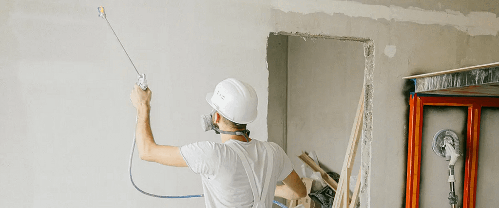 Contractor spraying paint on interior drywall