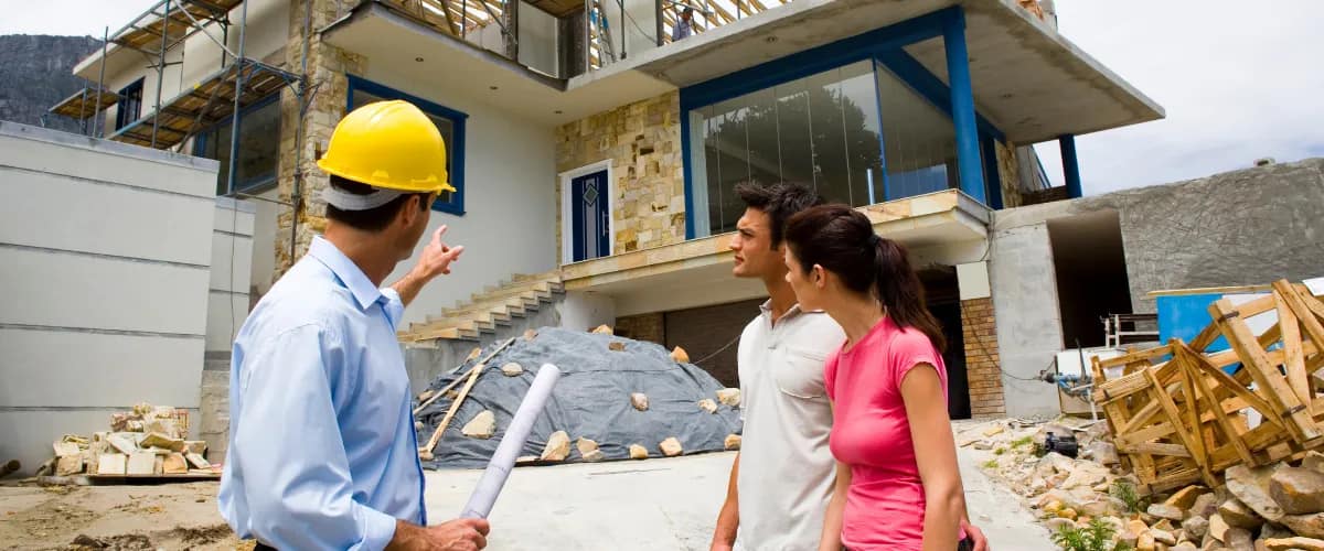 A construction inspector in a yellow hard hat showing a couple their new home under construction.