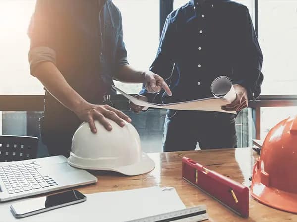 Construction professionals reviewing blueprints on a desk with a hard hat and level